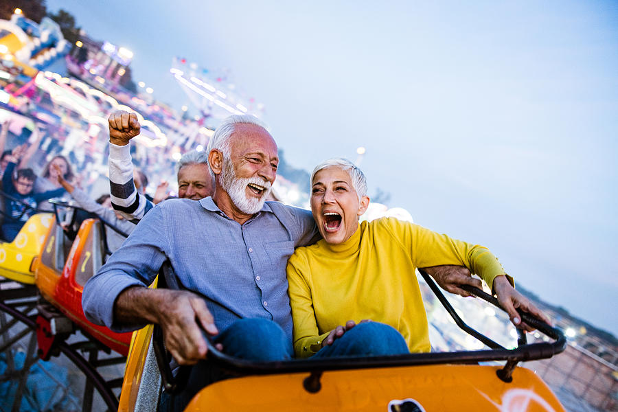 Carefree seniors having fun on rollercoaster at amusement park. Photograph by Skynesher