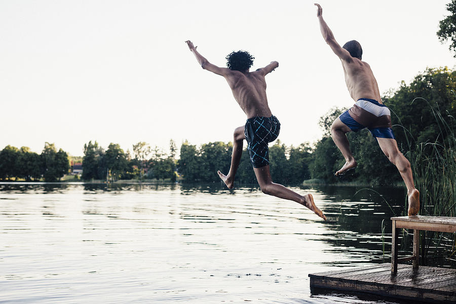 Carefree Summer Day: Teenagers Jumping Into A Lake Photograph by Fotografixx