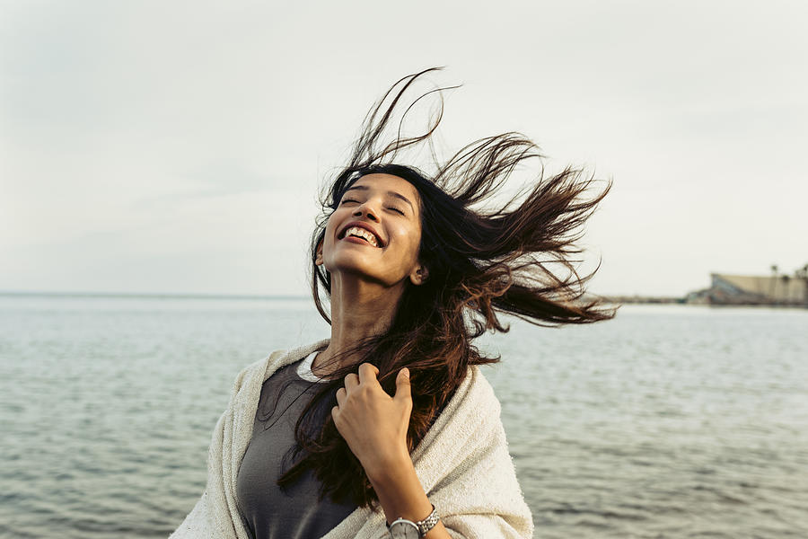 Carefree woman with tousled hair against sky at beach Photograph by Westend61