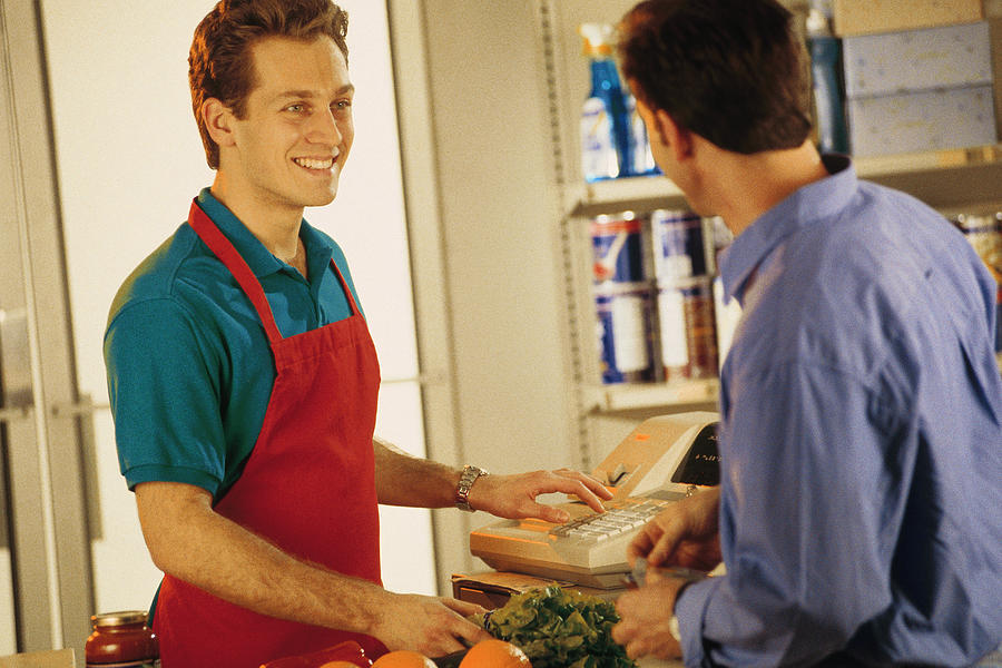 Cashier with customer at grocery store Photograph by Comstock
