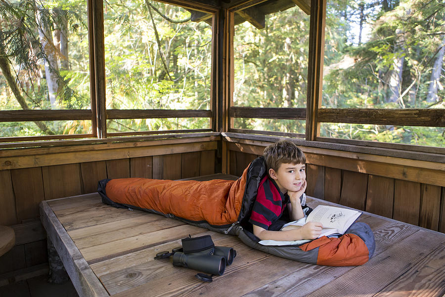 Caucasian boy reading in sleeping bag Photograph by Adam Crowley