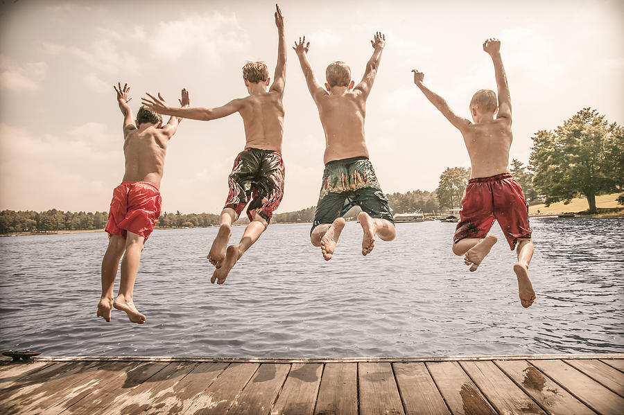 Caucasian boys jumping off wooden dock Photograph by Jon Feingersh Photography Inc