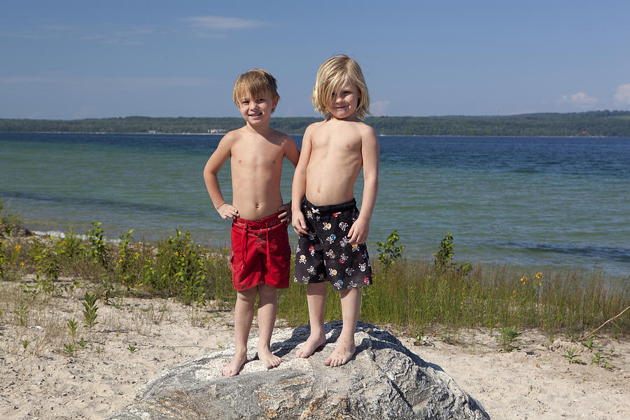 Caucasian boys standing on rock on beach Photograph by King Lawrence