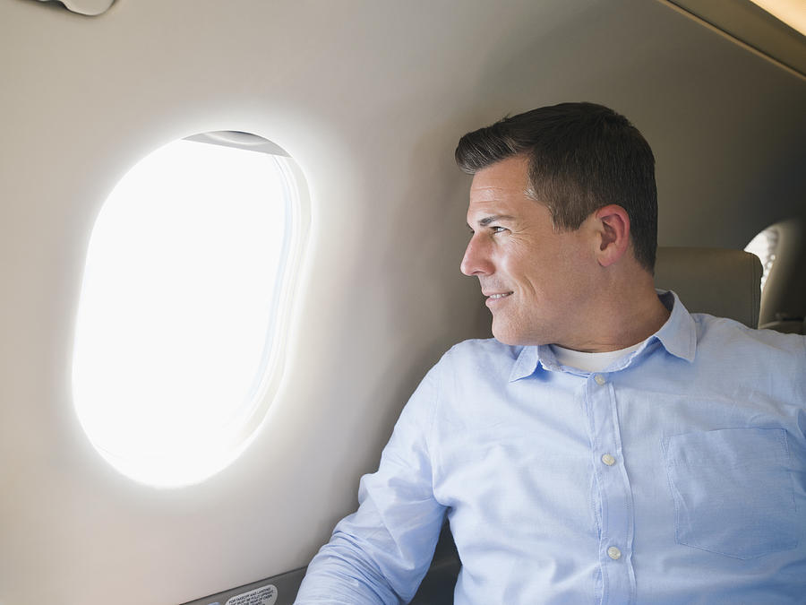 Caucasian businessman looking out airplane window Photograph by Erik Isakson