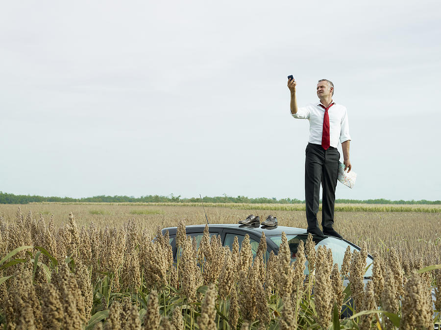 Caucasian businessman on top of car in field looking at gps device Photograph by Blend Images - Diego Cervo