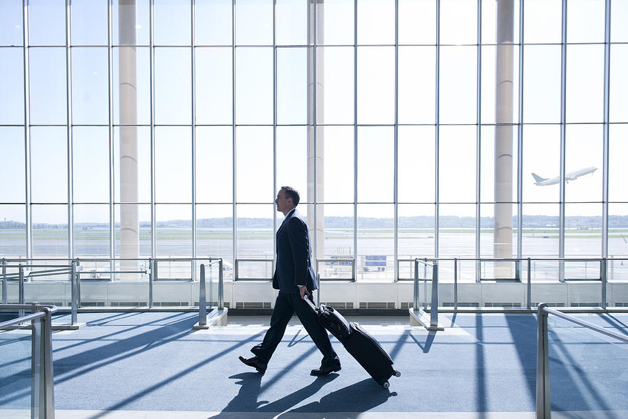 Caucasian businessman pulling luggage in airport Photograph by Jacobs Stock Photography Ltd