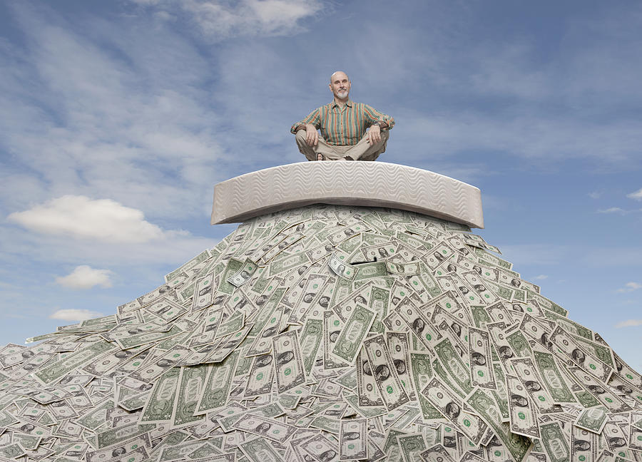Caucasian businessman sitting on mattress on mountain of money Photograph by John M Lund Photography Inc