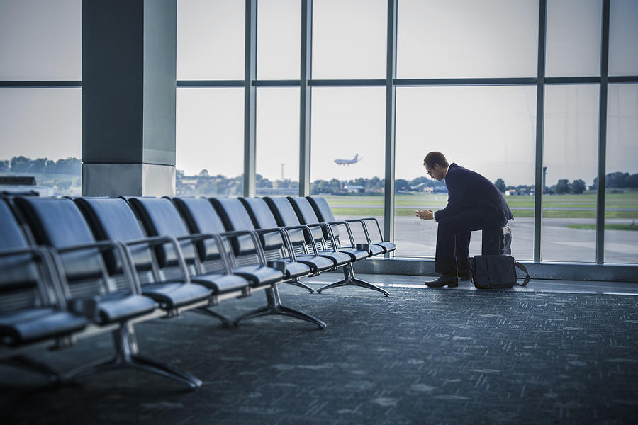 Caucasian businessman sitting suitcase in airport Photograph by John Fedele