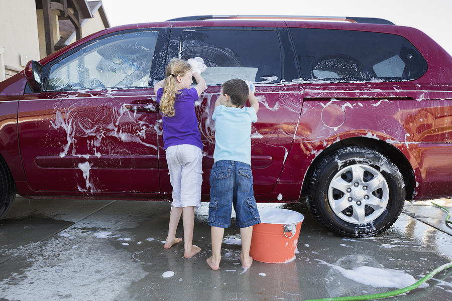 Caucasian children washing car in driveway Photograph by Mike Kemp