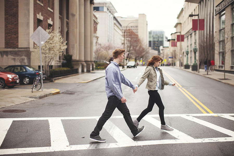 Caucasian couple holding hands crossing city intersection Photograph by Shestock