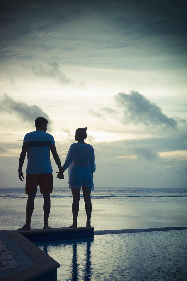 Caucasian couple holding hands near swimming pool at sunset Photograph by Jacobs Stock Photography Ltd