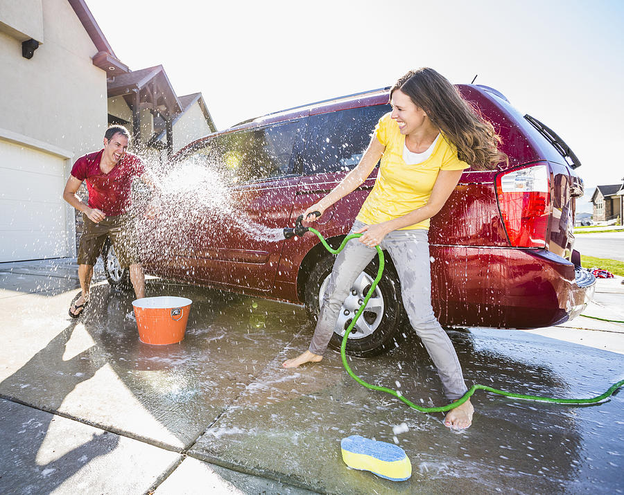 Caucasian couple playing while washing car in driveway Photograph by Mike Kemp