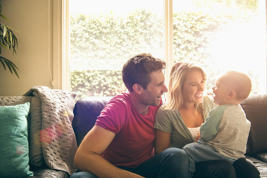 Caucasian couple playing with baby son on sofa Photograph by Jacobs Stock Photography Ltd