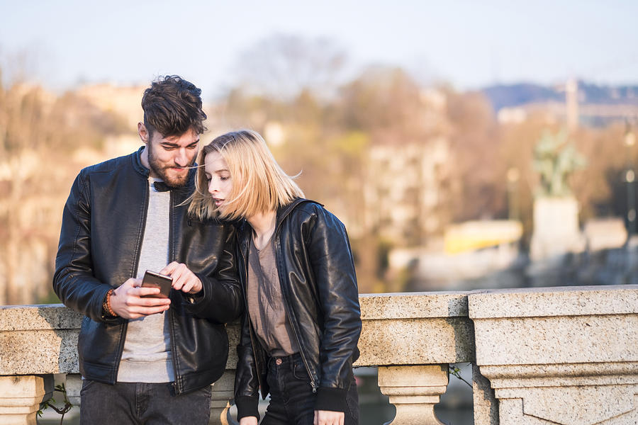 Caucasian couple texting on cell phone outdoors Photograph by Fabio Camandona