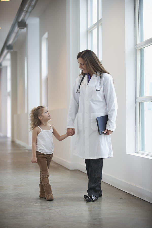 Caucasian doctor and girl holding hands in hallway Photograph by LWA/Dann Tardif