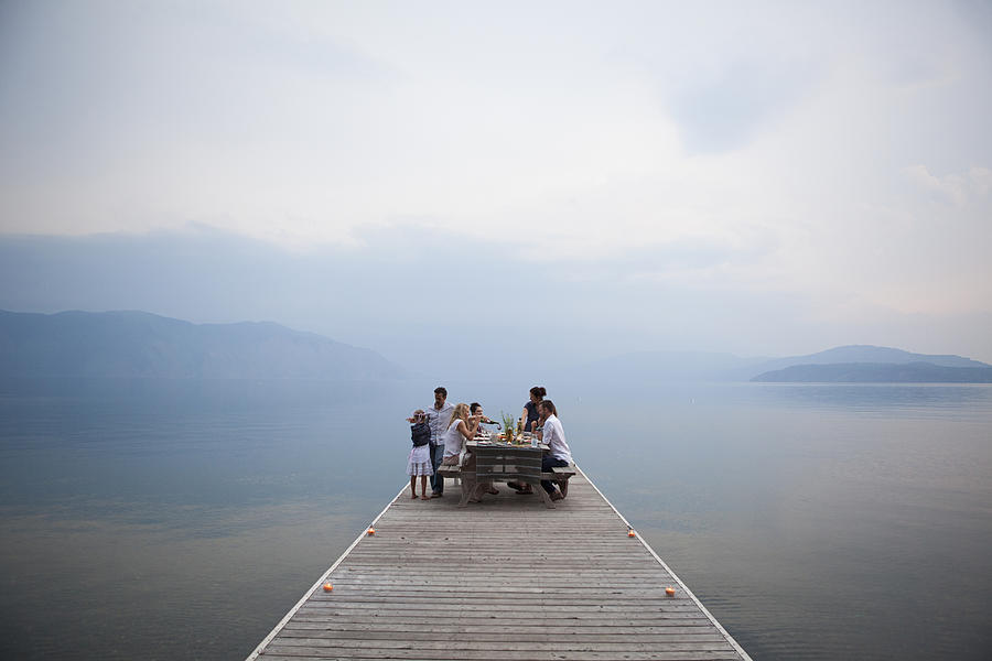 Caucasian family at picnic table on wooden dock over lake Photograph by Ronnie Kaufman