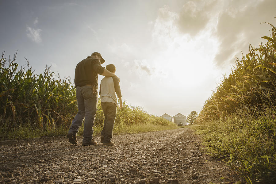 Caucasian father and son walking on dirt road through farm Photograph by John Fedele