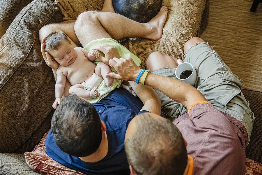 Caucasian gay couple holding sleeping baby boy on sofa Photograph by Inti St Clair