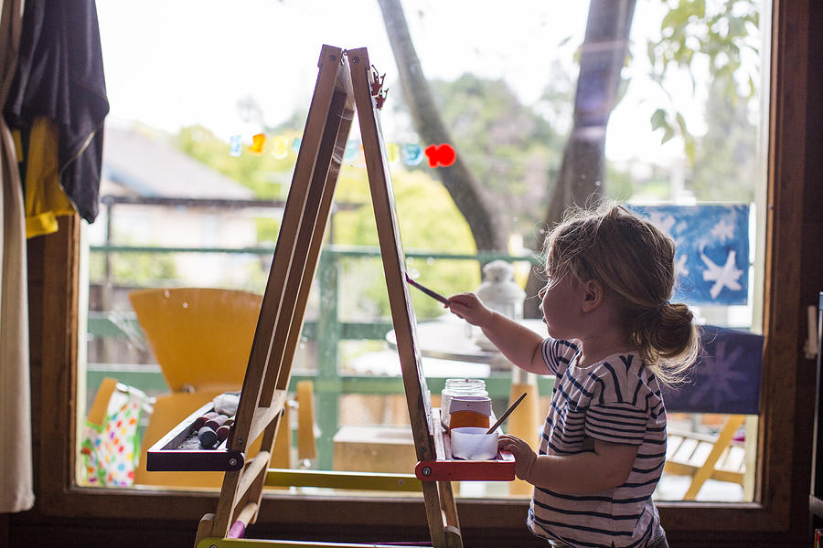 Caucasian girl painting on easel near window Photograph by Adam Hester