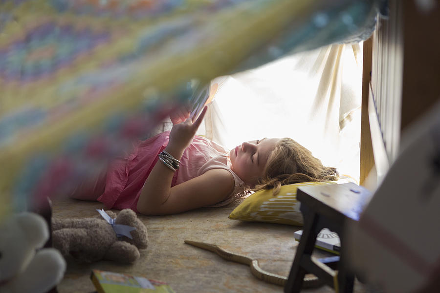 Caucasian girl reading in blanket fort Photograph by Marc Romanelli