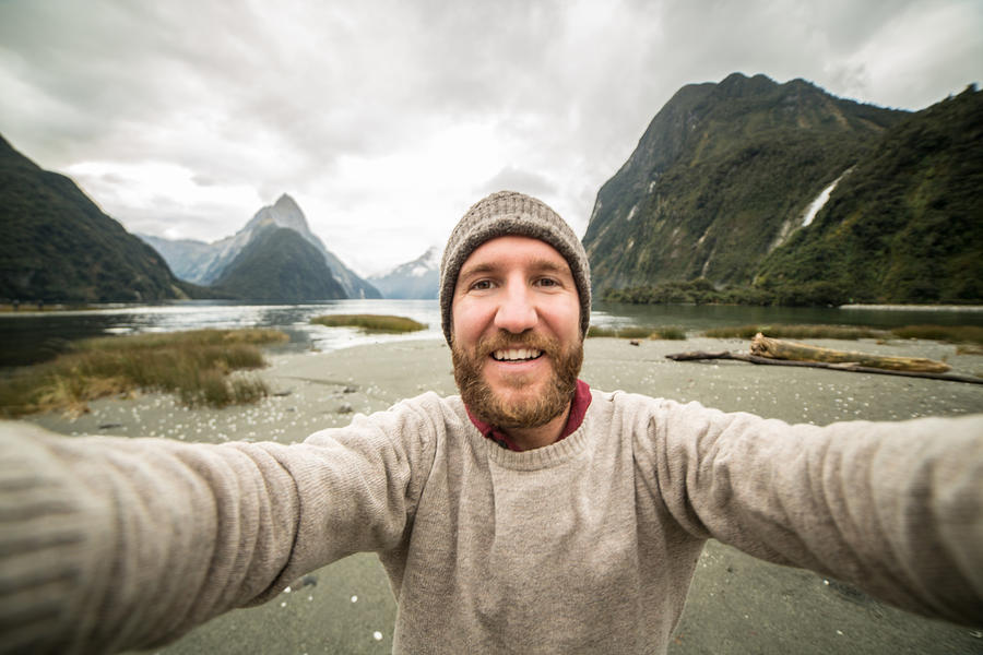 Caucasian male traveling takes selfie portrait with mountain landscape Photograph by Swissmediavision