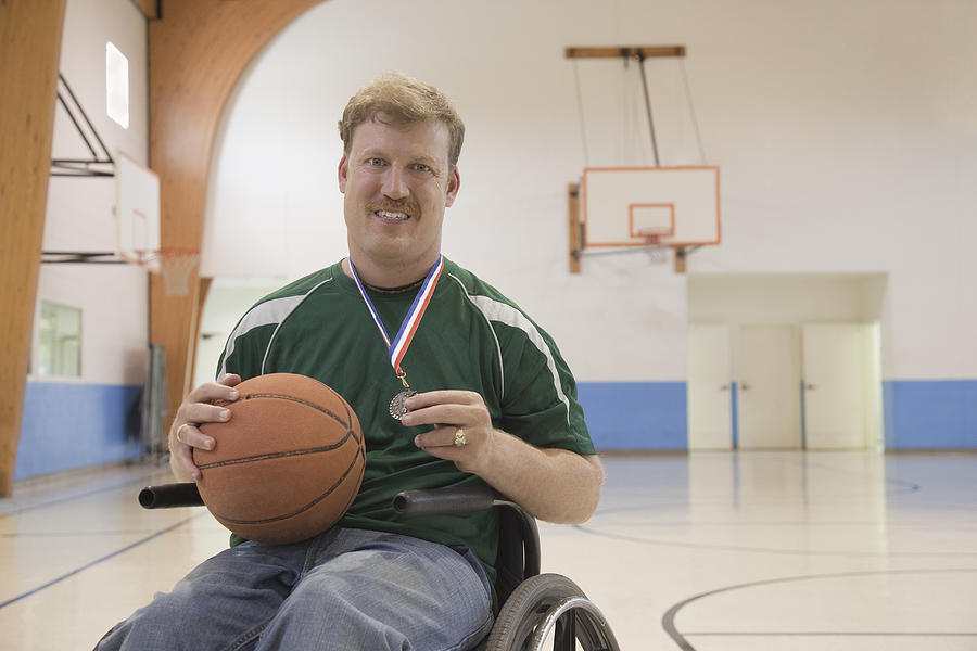 Caucasian man in wheelchair holding basketball medal Photograph by Terry Vine
