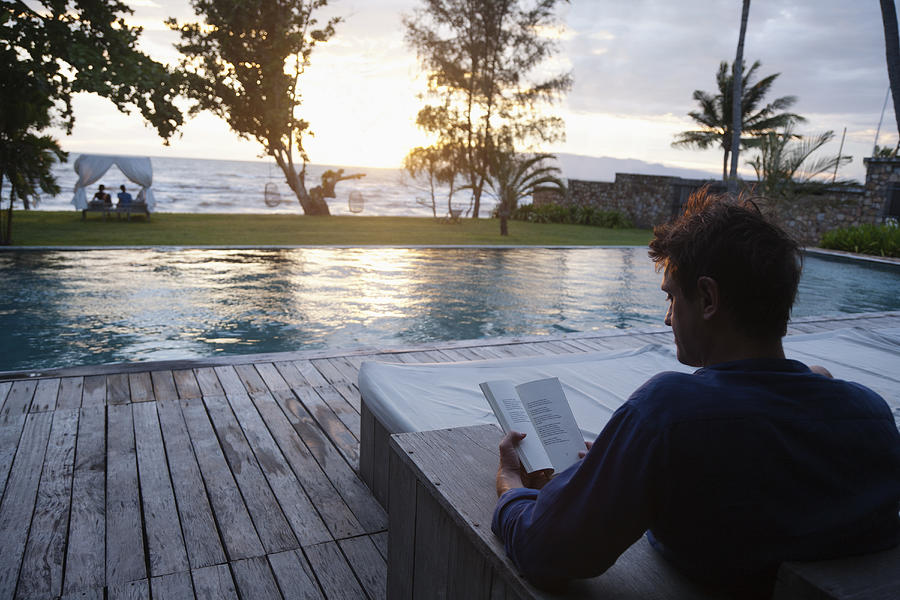 Caucasian man reading at poolside Photograph by Roberto Westbrook