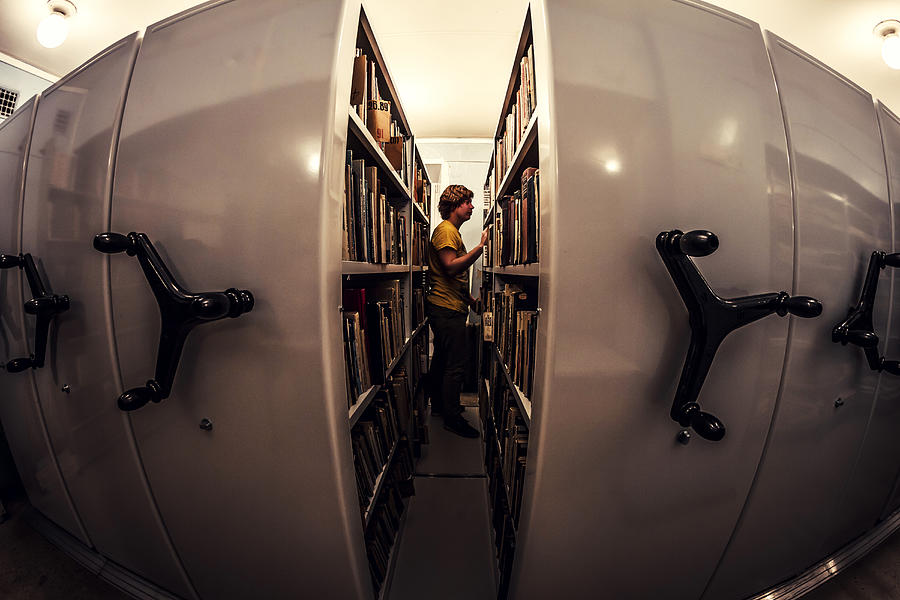 Caucasian man searching old newspapers in library archive Photograph by Maxim Chuvashov