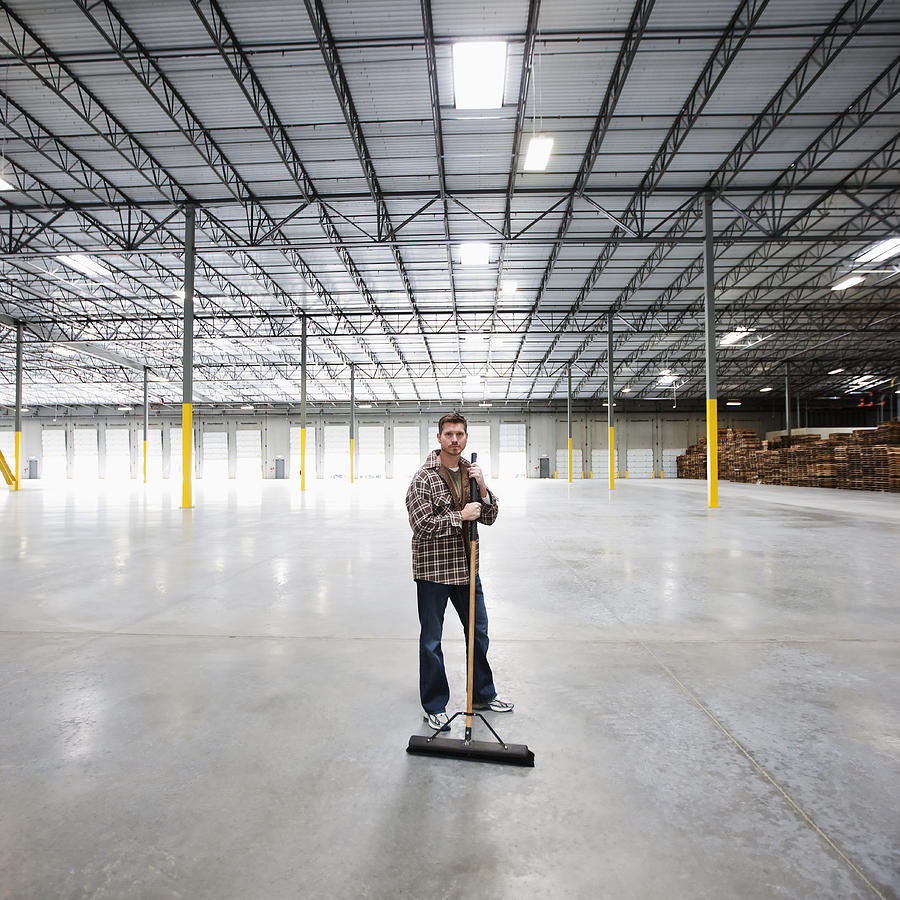 Caucasian man sweeping large, empty warehouse Photograph by Jetta Productions Inc