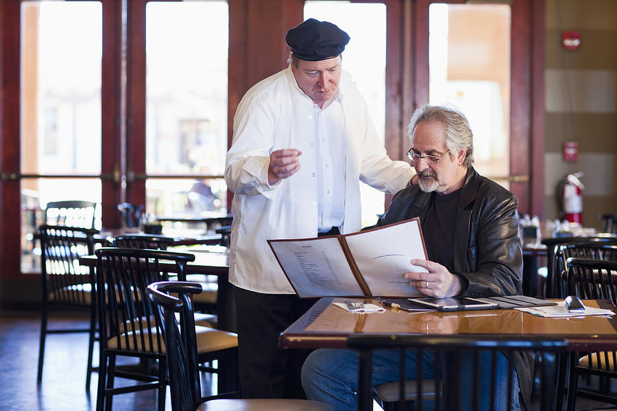 Caucasian man talking to chef in restaurant Photograph by Marc Romanelli