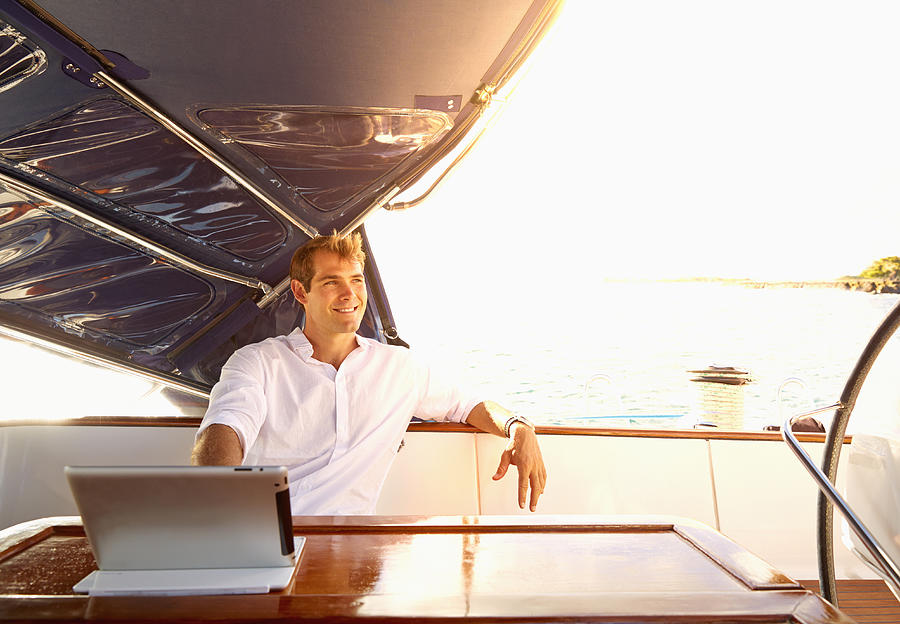 Caucasian man using digital tablet on yacht Photograph by Colin Anderson Productions pty ltd