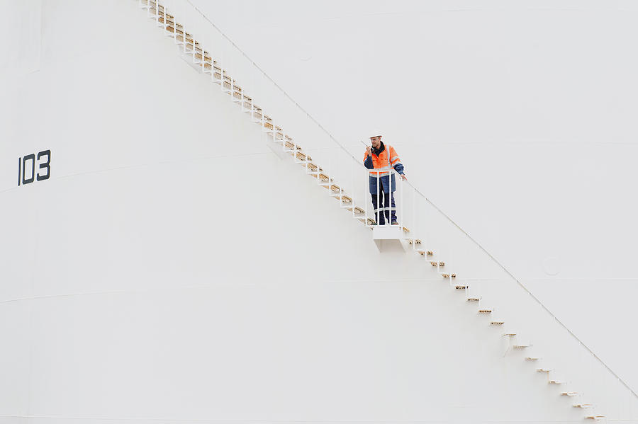 Caucasian technician using walkie-talkie on fuel storage tank staircase Photograph by Jacobs Stock Photography Ltd