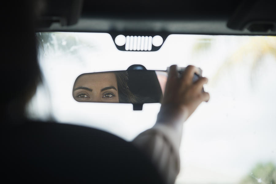 Caucasian woman adjusting rear view mirror in car Photograph by JGI/Jamie Grill