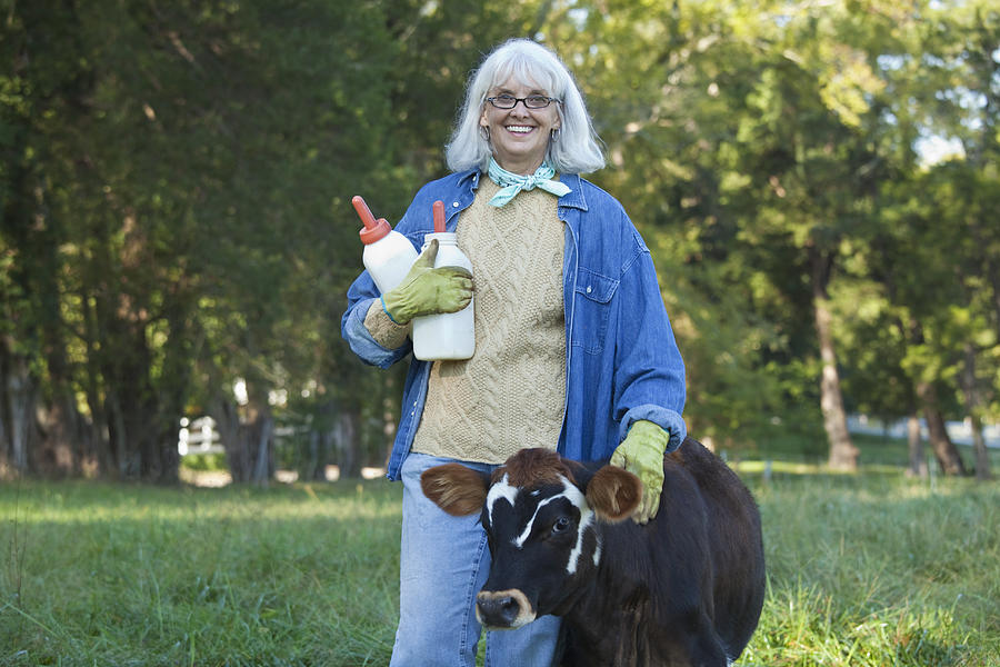 Caucasian woman holding bottles and petting calf Photograph by Ariel Skelley