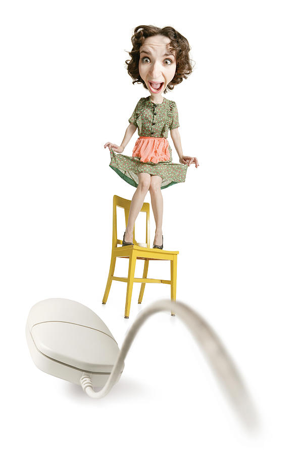 Caucasian Woman In 50s Housewife Clothes Stands On A Chair Terrified By A Computer Mouse Photograph by Photodisc