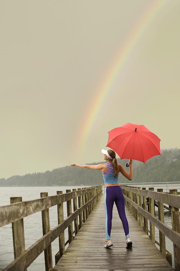 Caucasian woman in sportswear with red umbrella on pier catching rainbow Photograph by Pete Saloutos