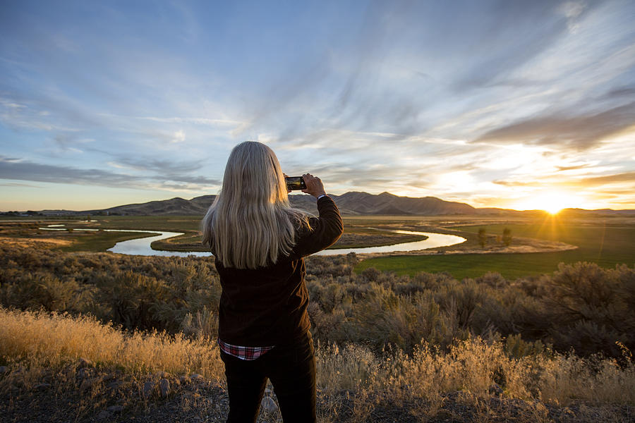 Caucasian woman photographing sunset over winding river Photograph by Steve Smith