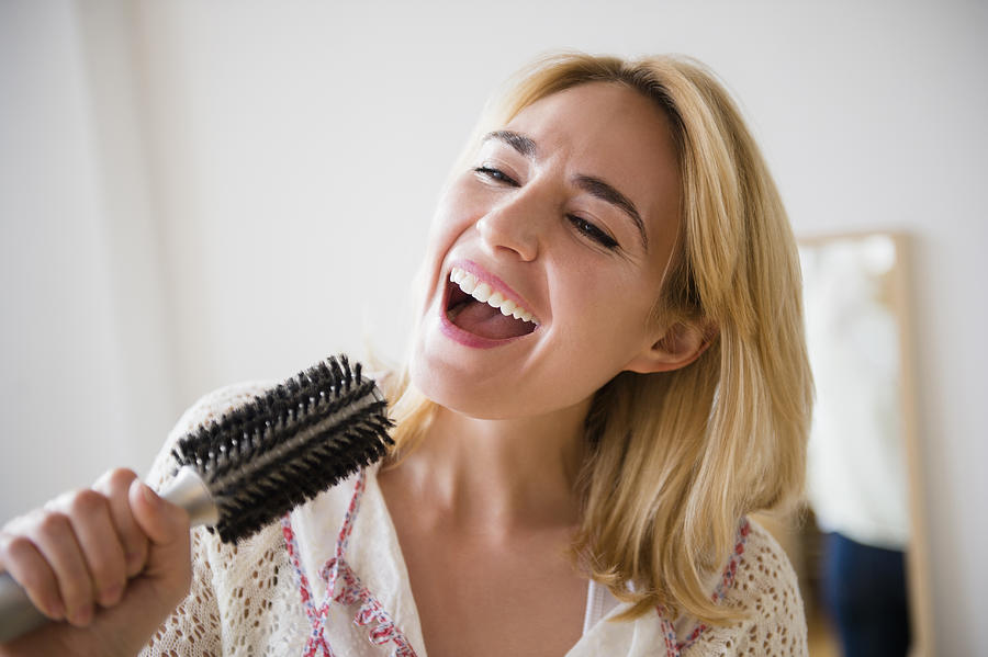 Caucasian woman singing into hairbrush Photograph by JGI/Jamie Grill