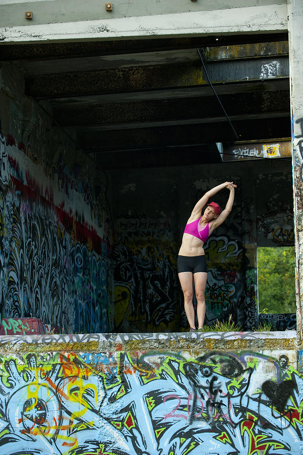 Caucasian woman stretching in abandoned loading dock Photograph by Pete Saloutos