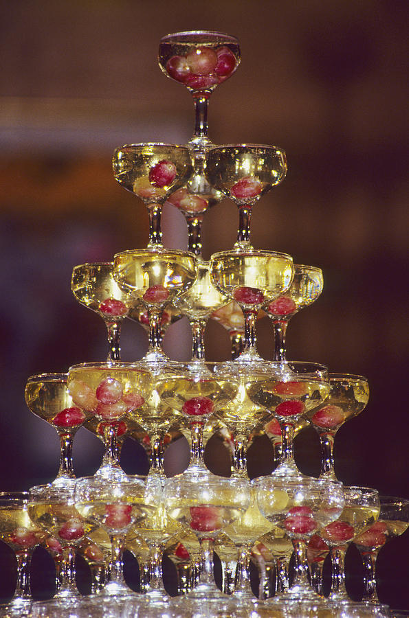 Champagne glass pyramid, glasses containing champagne and grapes Photograph by Stuart Gregory