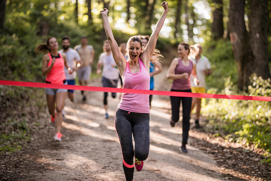 Cheerful athletic woman screaming while winning the marathon race in the forest. Photograph by Skynesher