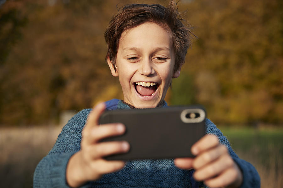 Cheerful boy using smart phone while taking selfie Photograph by Klaus Vedfelt