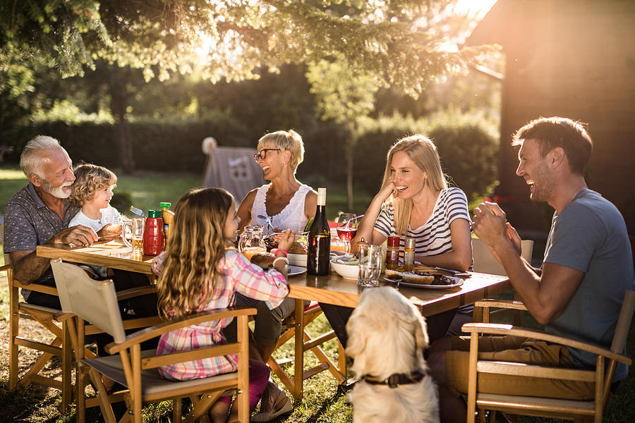 Cheerful extended family enjoying in conversation during lunch time in the backyard. Photograph by Skynesher