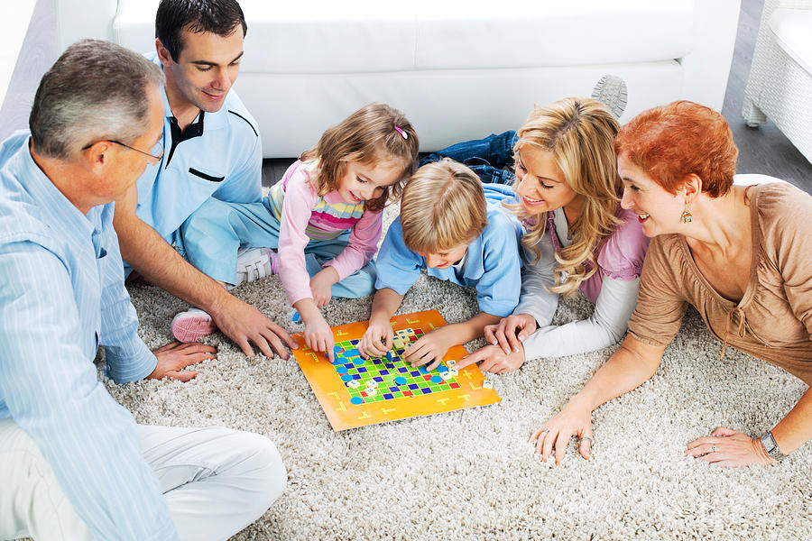 Cheerful extended family playing board game on the floor. Photograph by Skynesher
