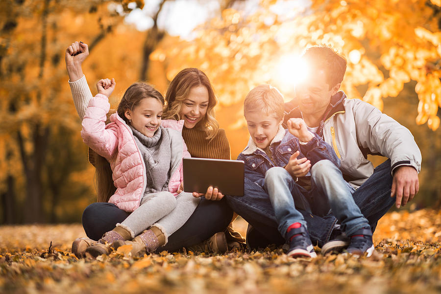 Cheerful family using digital tablet in autumn leaves. Photograph by BraunS