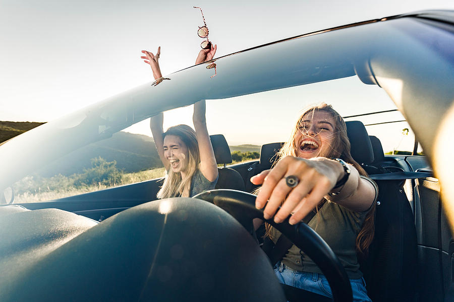 Cheerful female friends going on a trip in convertible car. Photograph by Skynesher
