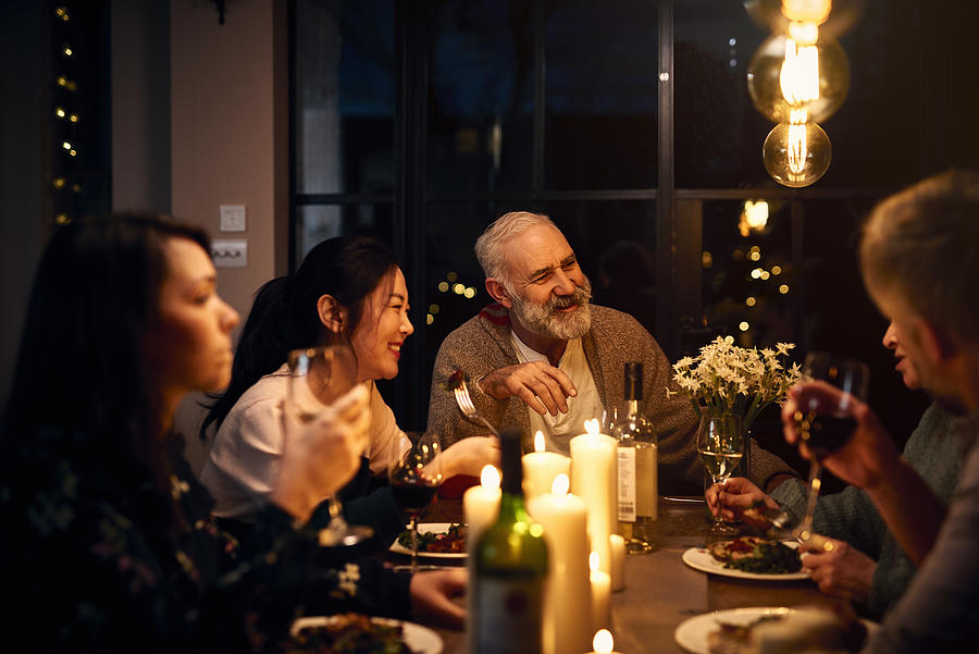 Cheerful guests at dinner table listening to friend and drinking wine Photograph by 10000 Hours