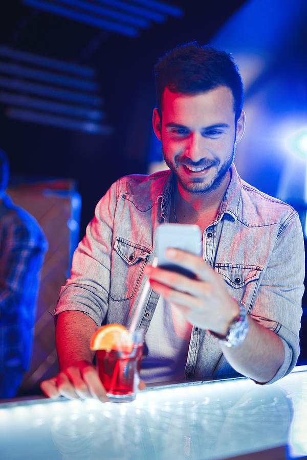 Cheerful man having cocktail while text messaging in nightclub Photograph by Emir Memedovski