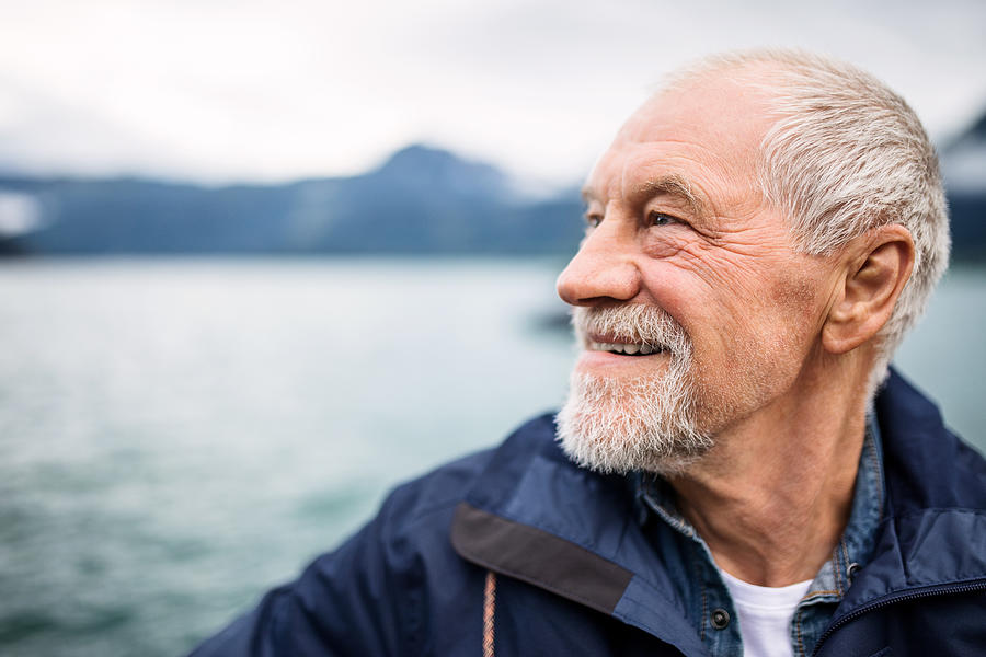 Cheerful senior man tourist standing by lake in nature on holiday. Photograph by Halfpoint Images