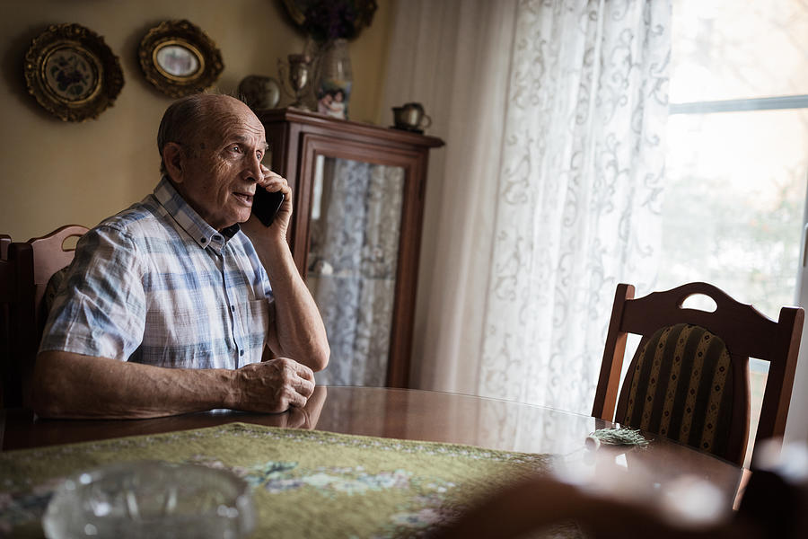 Cheerful senior man using mobile phone at home Photograph by Dobrila Vignjevic